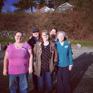 Group photo of the Upper Skagit Library employees smiling in a parking lot with bushes in the background.