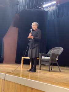 Photo of Nancy Pearl standing on an auditorium stage with a microphone in her hand.