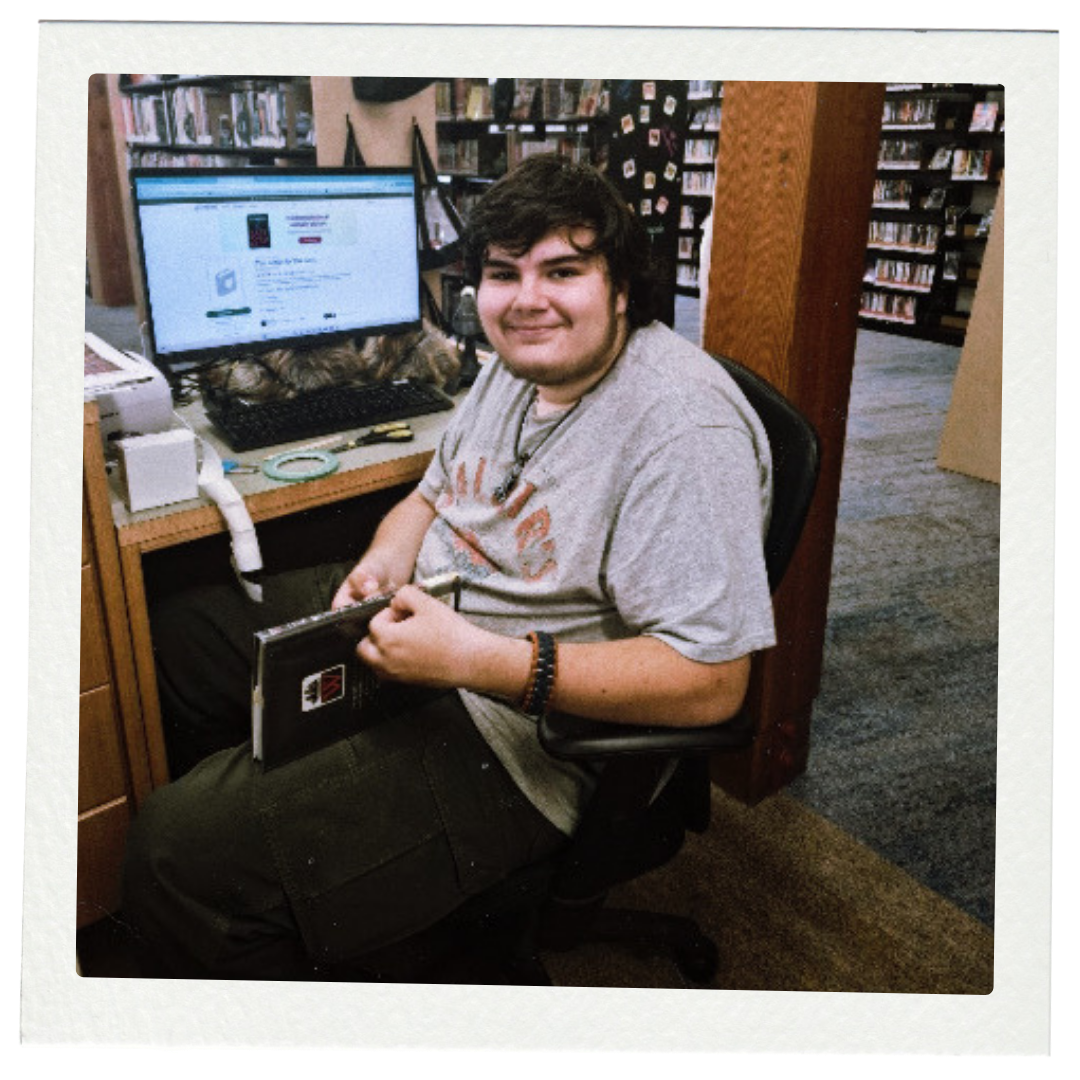 A grainy polaroid film style photo of a young man with black hair sitting in a chair near a computer desk.